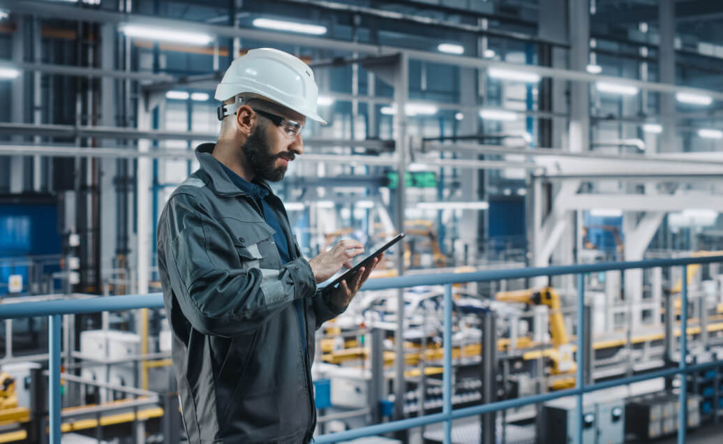 中年男子的安全gear looking at an iPad inside a factory