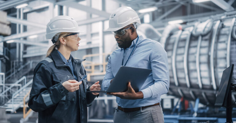 Two diverse professional heavy industry Engineers wearing safety Uniform and hard Hats working on laptop Computer.